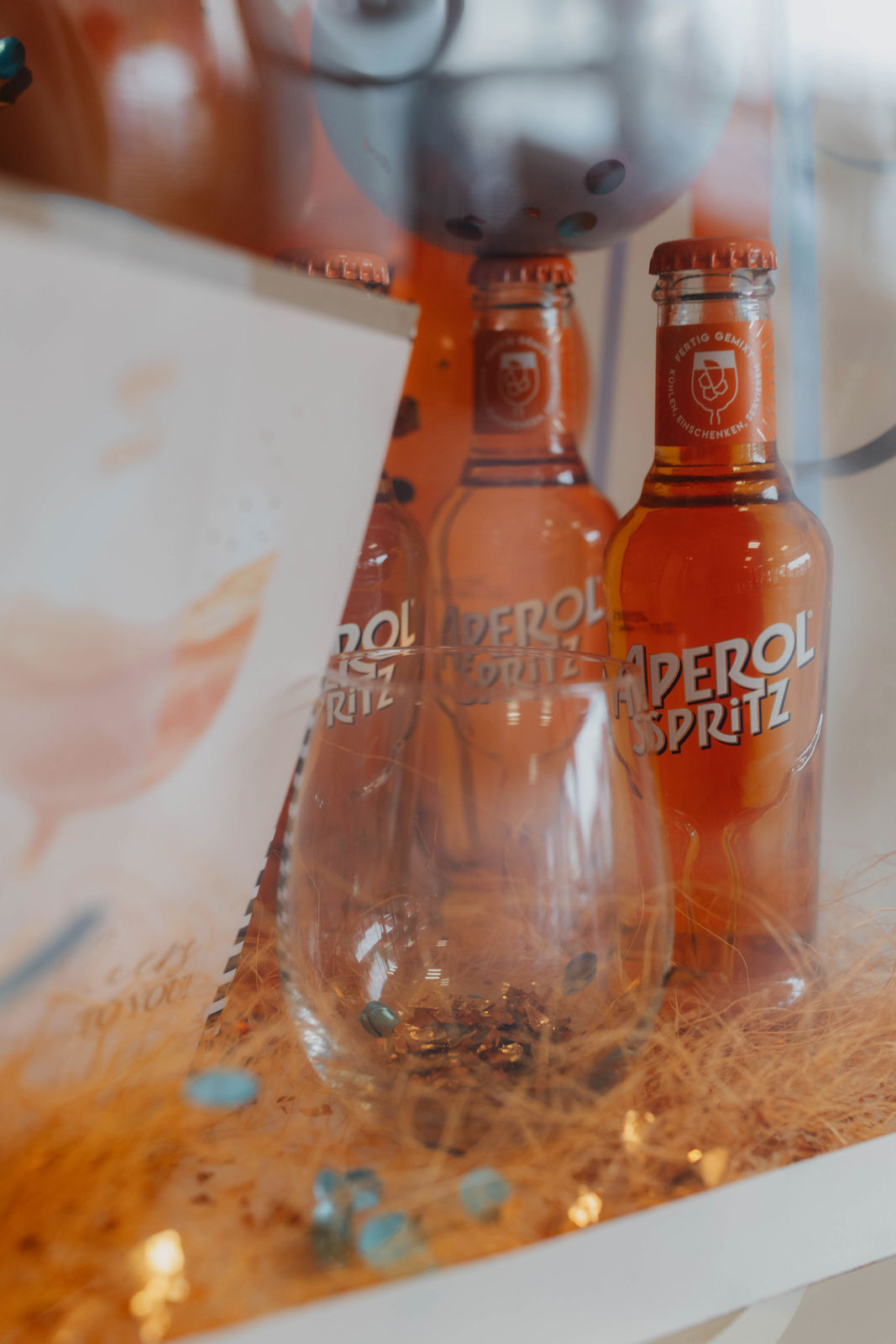 Zwei Aperol Spritz Flaschen in leuchtendem Orange neben einem leeren Glas