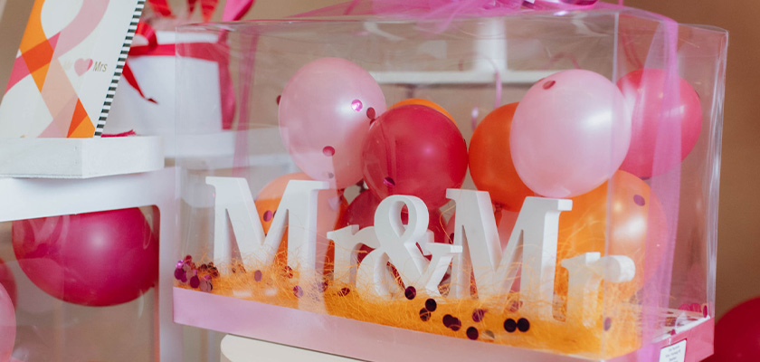 Eine durchsichtige Box mit der Aufschrift Mr und Mr, gefüllt mit rosa und roten Luftballons