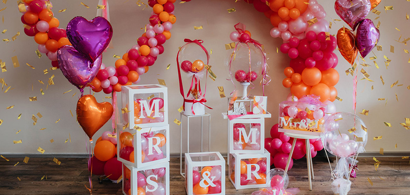 Bunte Ballondeko mit orangen und pinken Tönen sowie Herzballons und weißen Würfeln