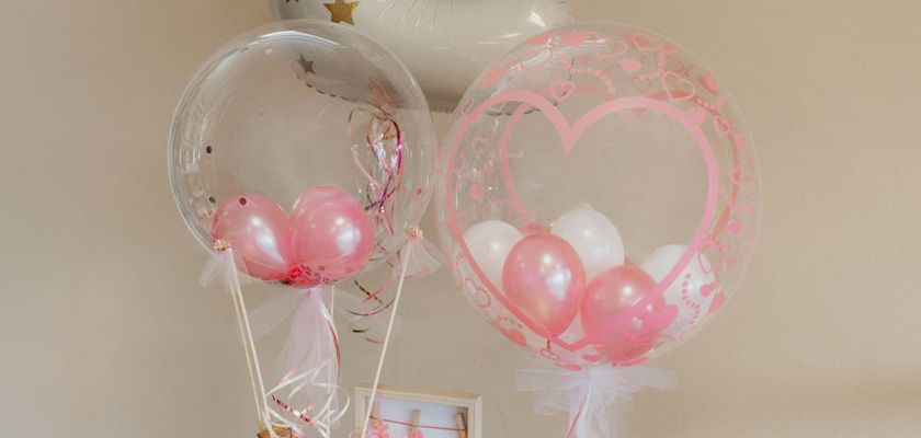 Zwei transparente Ballons mit rosa und weißen Herzluftballons schweben im Raum