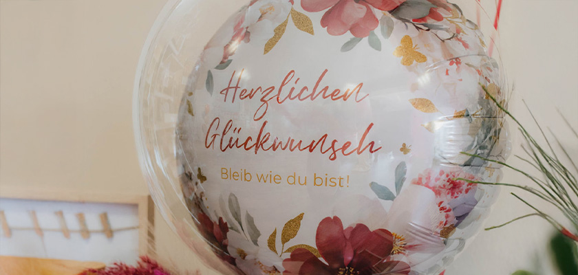 Ein durchsichtiger Ballon mit Blumenmotiv und der Aufschrift Herzlichen Glückwunsch