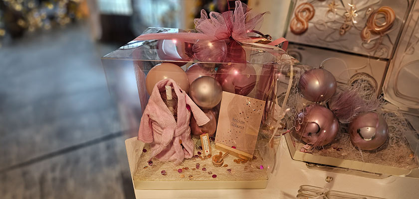 Eine Geschenkbox mit rosa und silbernen Kugeln, einem rosa Bademantel und Deko