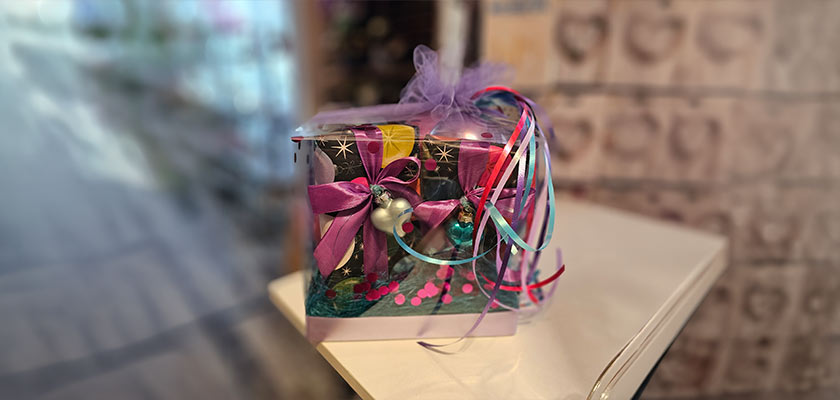 Das Bild zeigt eine farbenfrohe Geschenkbox mit Schleifen und bunten Bändern